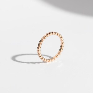 Puede incluir: Un delicado anillo de oro rosa con un dise&ntilde;o continuo de cuentas. El anillo est&aacute; sobre un fondo blanco limpio, con una sombra suave que a&ntilde;ade profundidad. Esta pieza minimalista es adecuada para el uso diario.