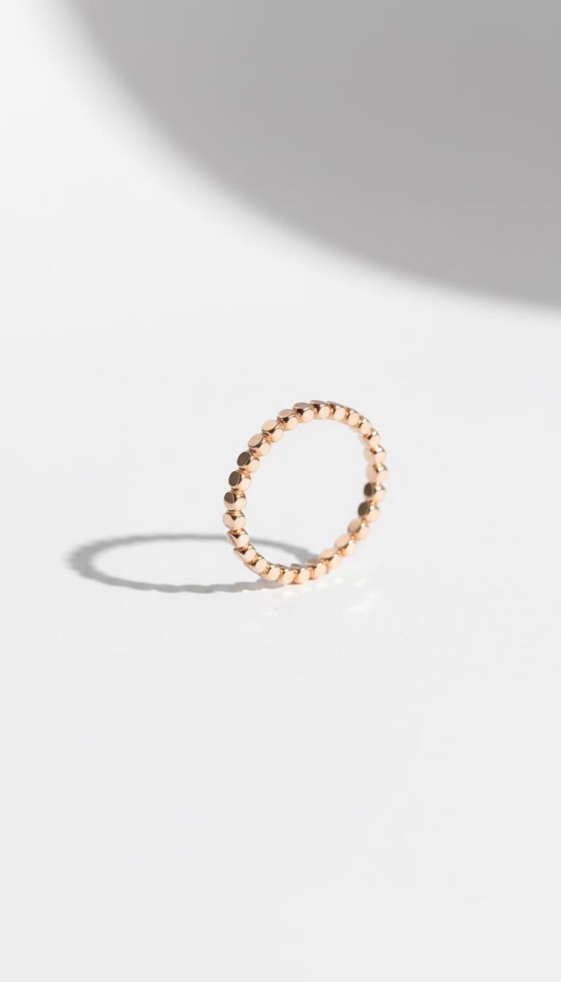 Puede incluir: Un delicado anillo de oro rosa con un dise&ntilde;o continuo de cuentas. El anillo est&aacute; sobre un fondo blanco limpio, con una sombra suave que a&ntilde;ade profundidad. Esta pieza minimalista es adecuada para el uso diario.
