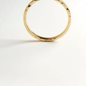 Puede incluir: Un anillo dorado con un dise&ntilde;o martillado. El anillo es circular y se encuentra sobre un fondo blanco. La superficie del anillo refleja la luz, resaltando su textura martillada. Esta joya es adecuada para el uso diario.