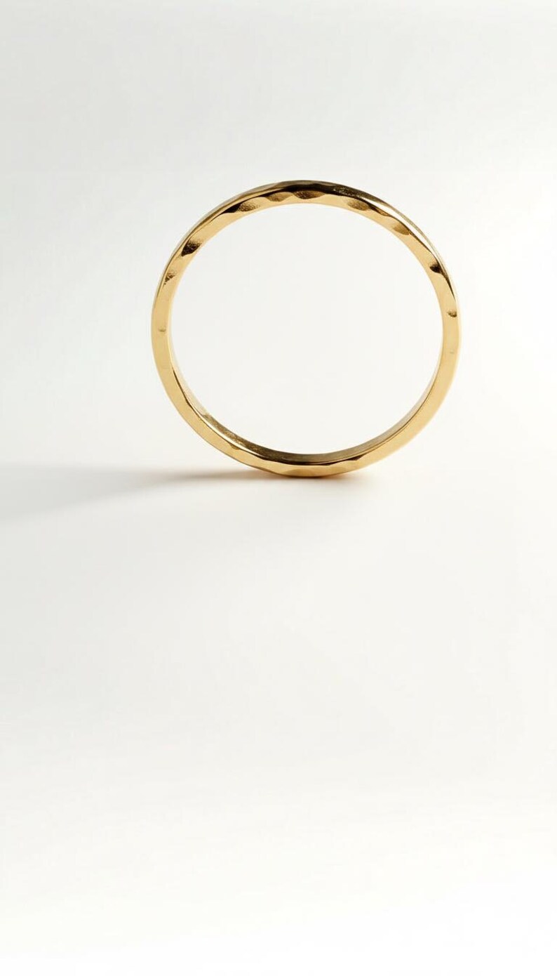 Puede incluir: Un anillo dorado con un dise&ntilde;o martillado. El anillo es circular y se encuentra sobre un fondo blanco. La superficie del anillo refleja la luz, resaltando su textura martillada. Esta joya es adecuada para el uso diario.