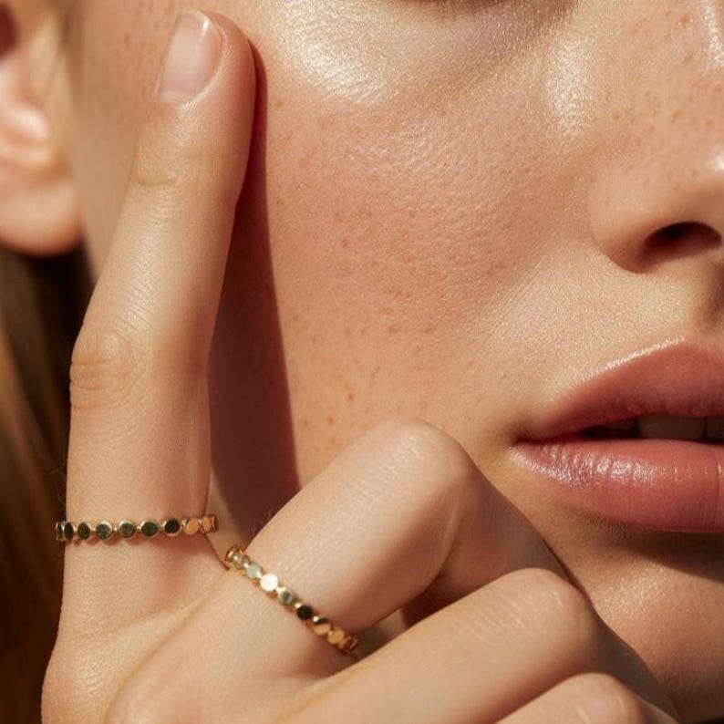 Puede incluir: Primer plano de dos anillos de oro con un dise&ntilde;o punteado. Un anillo est&aacute; en un dedo y el otro en otro dedo. Los anillos son finos y delicados, con un patr&oacute;n repetitivo de peque&ntilde;os puntos circulares.