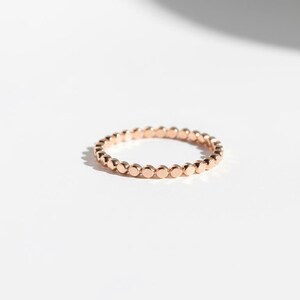 Puede incluir: Un delicado anillo de oro rosa con una serie de peque&ntilde;os acentos circulares espaciados uniformemente. El anillo se encuentra sobre un fondo blanco limpio, resaltando su simple elegancia. El dise&ntilde;o del anillo es minimalista y moderno.