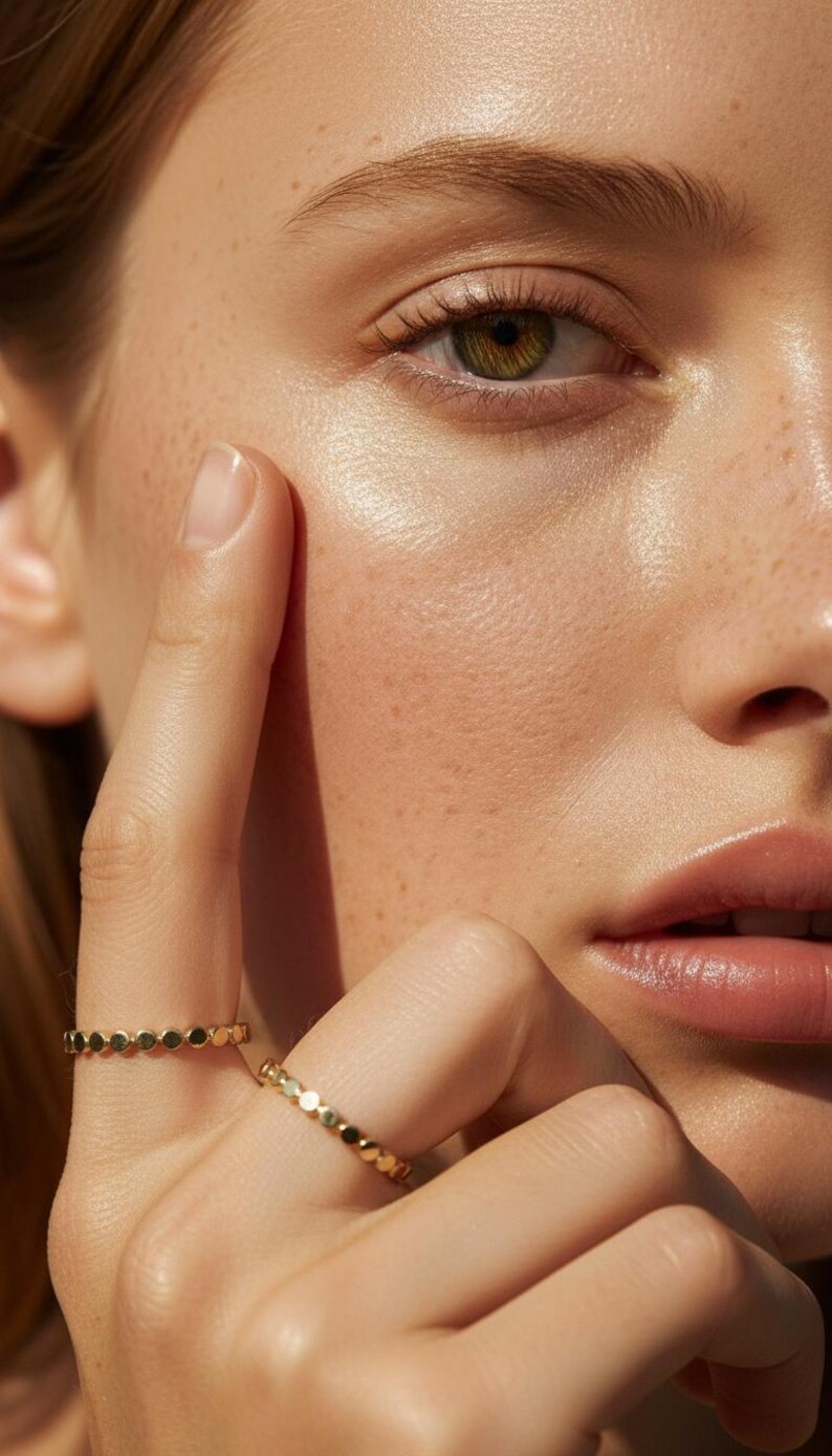 Puede incluir: Primer plano de un rostro con un anillo de oro en el dedo. El anillo presenta una serie de peque&ntilde;as formas circulares conectadas. La piel tiene pecas y un brillo saludable. El ojo es verde y los labios son de un rosa natural.