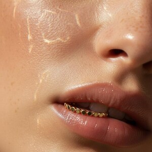 Puede incluir: Primer plano de un rostro con un anillo labial dorado. El anillo est&aacute; hecho de peque&ntilde;as cuentas redondas doradas. Los labios de la persona son brillantes y la piel tiene un aspecto h&uacute;medo.