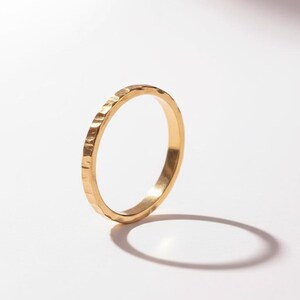 Puede incluir: Un anillo de oro con una superficie texturizada. El anillo est&aacute; sobre un fondo blanco, con una sombra proyectada hacia la derecha. El dise&ntilde;o del anillo presenta una textura martillada, d&aacute;ndole un aspecto &uacute;nico. Este anillo es una joya.