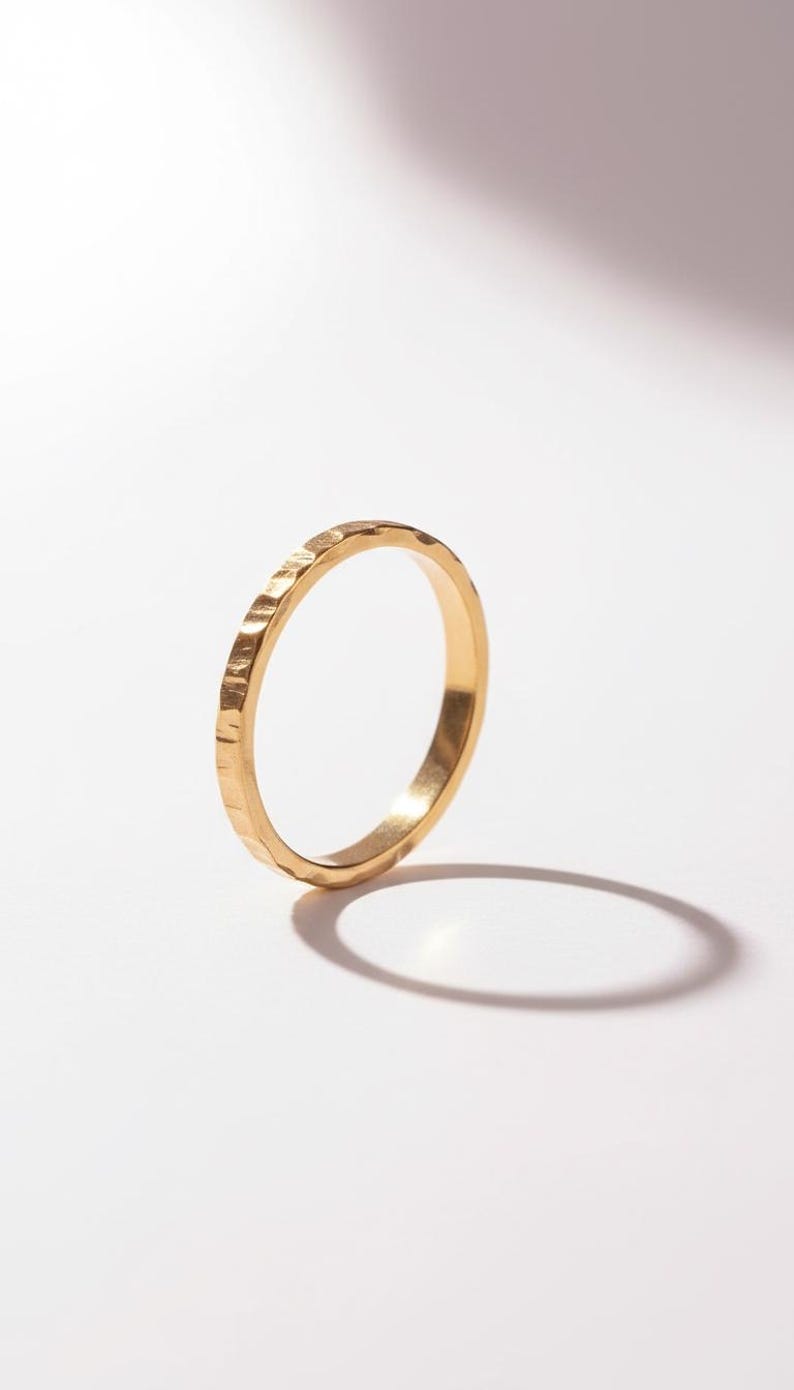 Puede incluir: Un anillo de oro con una superficie texturizada. El anillo est&aacute; sobre un fondo blanco, con una sombra proyectada hacia la derecha. El dise&ntilde;o del anillo presenta una textura martillada, d&aacute;ndole un aspecto &uacute;nico. Este anillo es una joya.