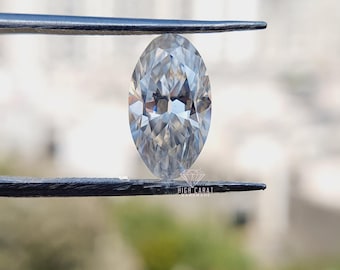 May include: A clear, colorless, marquise-cut gemstone held between two dark metal tweezers. The stone features a faceted surface that reflects light with a brilliant, multi-faceted pattern. The text HIGH CARAT HANDMADE is visible on the lower tweezer.