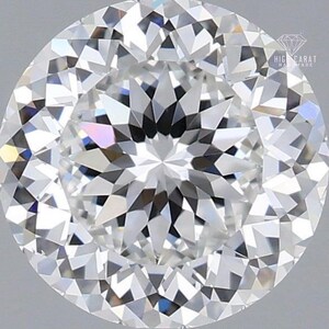 Puede incluir: Un diamante de talla brillante redonda con numerosas facetas triangulares y en forma de cometa que reflejan la luz. La piedra es clara e incolora con un alto nivel de brillo interno. El texto HIGH CARAT HANDMADE es visible en la esquina superior derecha.