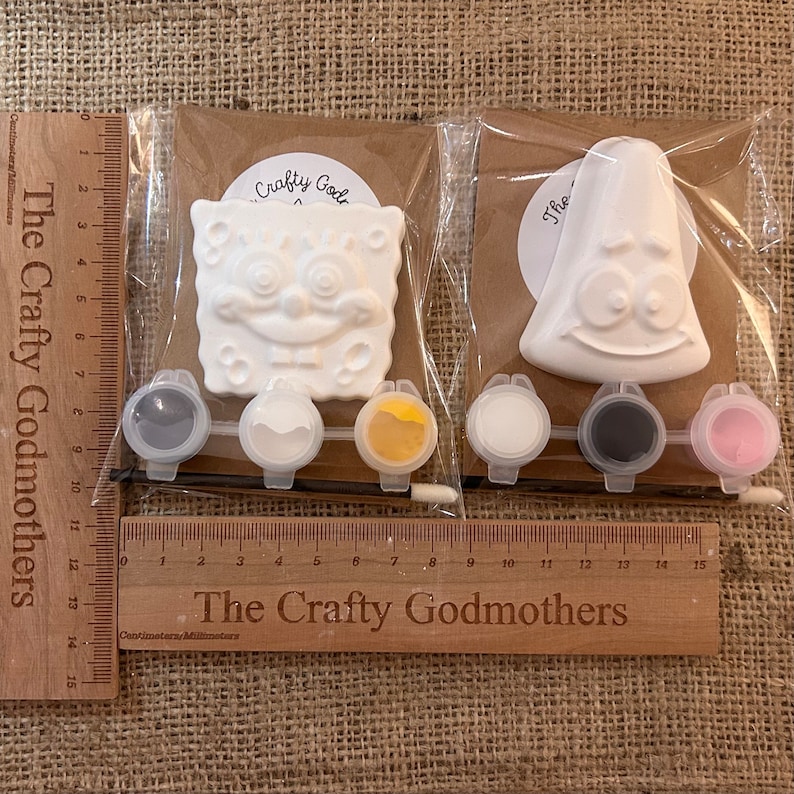 May include: Two paint-your-own character kits featuring SpongeBob SquarePants and Patrick Star. Each kit includes a white ceramic figure, four small paint pots, and a paintbrush.