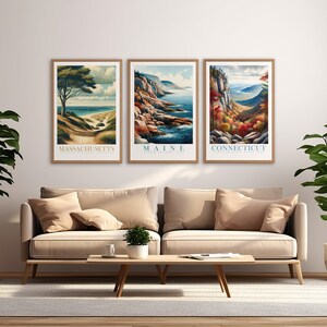 May include: Three framed landscape posters with scenic views of Massachusetts, Maine, and Connecticut. Each poster features a different natural landscape, including a beach, a rocky coastline, and a mountain range. The posters are arranged in a row on a white wall.