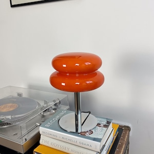 Marshmallow Tischlampe in Orange von GLOW UP STUDIO, stilvoll platziert auf Büchern.