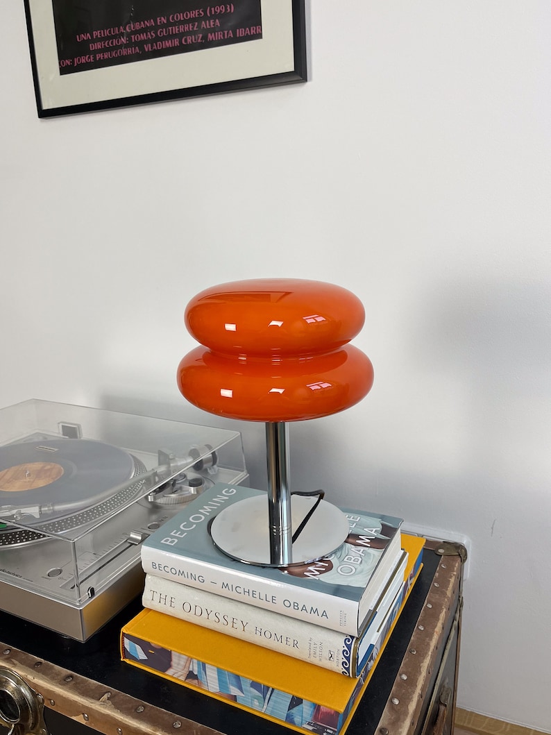Marshmallow Tischlampe in Orange von GLOW UP STUDIO, stilvoll platziert auf Büchern.