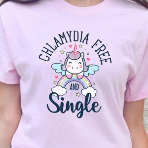May include: Pink t-shirt with a graphic of a unicorn on a rainbow with the text "Chlamydia Free and Single".