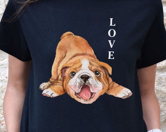 Puede incluir: Camiseta negra con una ilustración de dibujos animados de un bulldog marrón y blanco acostado boca abajo. La palabra "LOVE" está impresa verticalmente en el lado derecho de la camiseta.