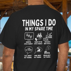 May include: Black t-shirt with white text and graphics. The text reads "THINGS I DO IN MY SPARE TIME" with illustrations of stock market activities. Includes phrases like "Monitor Stock Market" and "Dream About Day Trading."