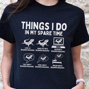 Può includere: Maglietta nera con testo bianco che recita "Things I do in my spare time". Il testo è circondato da illustrazioni di draghi barbuti in varie attività, tra cui guardare, uscire con, ricercare, parlare di, pensare a e sognare draghi barbuti.