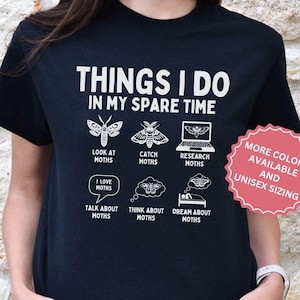 May include: Black t-shirt with white text that reads "Things I do in my spare time" and features a series of illustrations of moths. The illustrations include a moth with a magnifying glass, a moth with a net, a moth with a laptop, a speech bubble that says "I love moths", a moth with a thought bubble, a moth with a bed, and the text "Look at moths", "Catch moths", "Research moths", "Talk about moths", "Think about moths", and "Dream about moths". The t-shirt also has a pink circle with white text that reads "More colors available and unisex sizing".