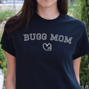 May include: Black t-shirt with white text that reads "BUGG MOM" and a heart with a paw print inside.