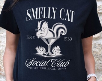 May include: Black t-shirt featuring a white graphic of a squirrel in a martini glass. The text "Smelly Cat Est. 1939 Social Club Beverly Hills, California" is printed on the shirt.