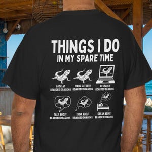May include: Black t-shirt with white text and graphics. The text reads "THINGS I DO IN MY SPARE TIME" above illustrations of bearded dragons. The graphics depict activities like looking at, hanging out with, and researching bearded dragons.