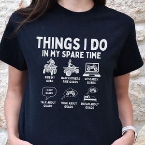 May include: Black t-shirt with white text that reads "Things I do in my spare time". The text is surrounded by illustrations of ATVs and related activities, including "Ride my Quad", "Watch others ride quads", "Research quads", "I love quads", "Talk about quads", "Think about quads", and "Dream about quads".