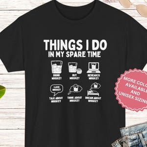 May include: A black t-shirt featuring white text that reads THINGS I DO IN MY SPARE TIME, accompanied by six white graphic icons depicting a glass of whiskey, a bottle, a laptop, a speech bubble, a thought bubble, and a person sleeping in a bed.
