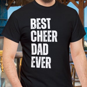 Op de afbeelding: Zwart T-shirt met witte tekst die "Best Cheer Dad Ever" zegt.