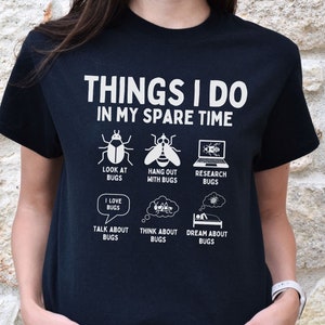 May include: Black t-shirt with white text that reads "Things I do in my spare time". The text is surrounded by illustrations of bugs, including a beetle, a fly, a laptop, a speech bubble with the words "I love bugs", and a thought bubble with the words "Think about bugs".