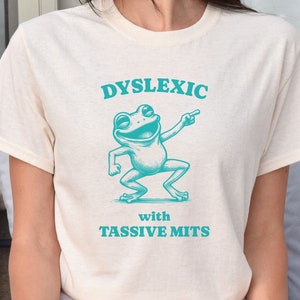 May include: A white t-shirt with a teal green frog graphic and the text "Dyslexic with Tassivve Mits".