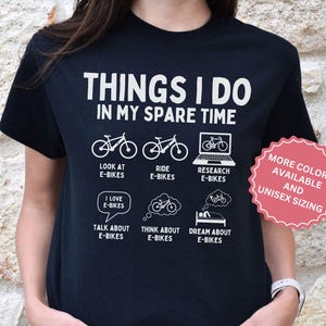 Puede incluir: Una camiseta negra con texto blanco que dice THINGS I DO IN MY SPARE TIME. Debajo del texto hay seis iconos con las etiquetas: LOOK AT E-BIKES, RIDE E-BIKES, RESEARCH E-BIKES, TALK ABOUT E-BIKES, THINK ABOUT E-BIKES y DREAM ABOUT E-BIKES.