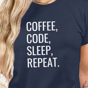 Op de afbeelding: Een marineblauw t-shirt met witte tekst die "COFFEE, CODE, SLEEP, REPEAT." luidt.