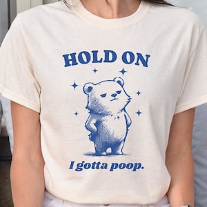May include: A white t-shirt with a blue illustration of a bear with the text "HOLD ON I gotta poop."