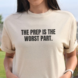 May include: A beige t-shirt with the text "THE PREP IS THE WORST PART." printed in black.