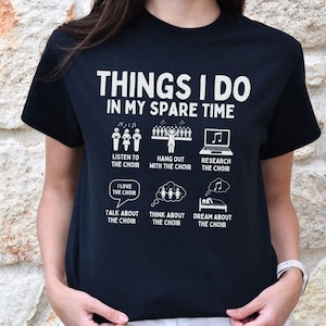 以下が含まれることがあります： 「Things I do in my spare time」という白い文字が書かれた黒いTシャツ。テキストには、歌っている人々、音符、ラップトップ、ベッドのイラストが添えられています。