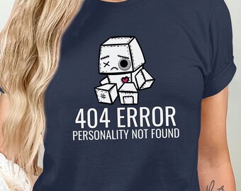 Puede incluir: Una camiseta azul marino con un robot de dibujos animados blanco con cara triste y el texto "404 ERROR PERSONALITY NOT FOUND".