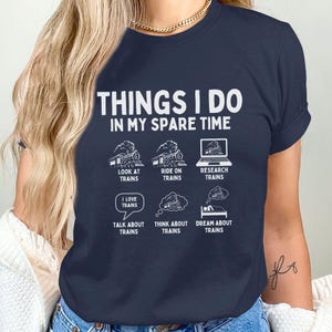 May include: A navy blue t-shirt with the text "Things I do in my spare time" and a series of illustrations of trains. The illustrations depict looking at trains, riding on trains, researching trains, talking about trains, thinking about trains, and dreaming about trains.