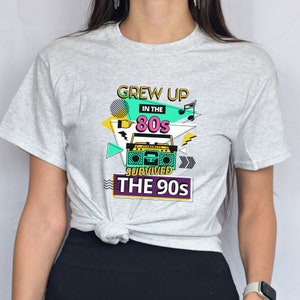 May include: Gray t-shirt with a graphic design featuring a boombox, musical notes, and the text "Grew Up In The 80s Survived The 90s".