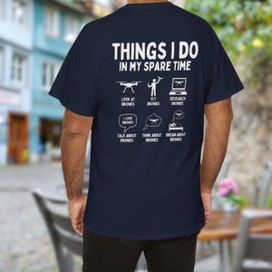 Pode incluir: Camiseta azul marinho com texto e ilustra&ccedil;&otilde;es brancas sobre drones. O texto diz "THINGS I DO IN MY SPARE TIME" com ilustra&ccedil;&otilde;es de drones e atividades relacionadas, como voar, pesquisar e sonhar com drones.