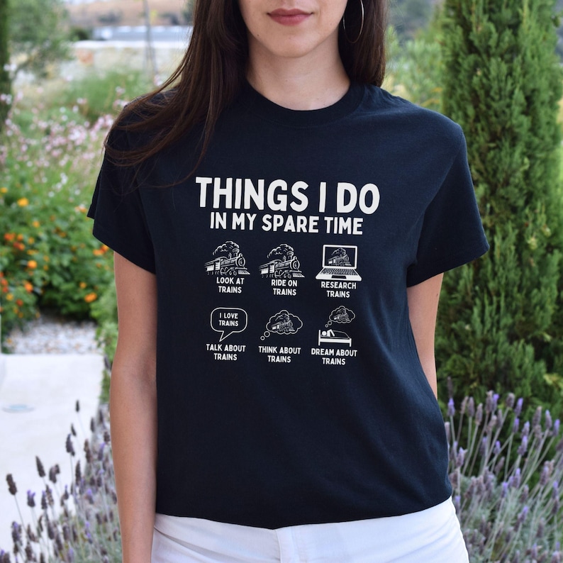 May include: A black t-shirt with white text that reads "Things I do in my spare time". The text is surrounded by illustrations of trains and train-related activities, such as looking at trains, riding on trains, researching trains, loving trains, talking about trains, thinking about trains, and dreaming about trains.