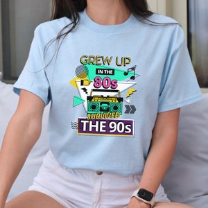 May include: Light blue t-shirt with a graphic design featuring a boombox, music notes, and the text "Grew Up In The 80s Survived The 90s".