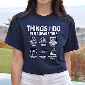 May include: A navy blue t-shirt with a white graphic that says "Things I do in my spare time" and lists activities related to trains. The graphic includes illustrations of trains, a laptop, and a sleeping person.