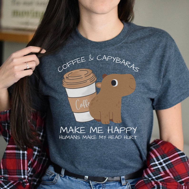 May include: A dark blue t-shirt with a cartoon illustration of a coffee cup and a capybara. The text on the shirt reads "Coffee & Capybaras Make Me Happy Humans Make My Head Hurt."
