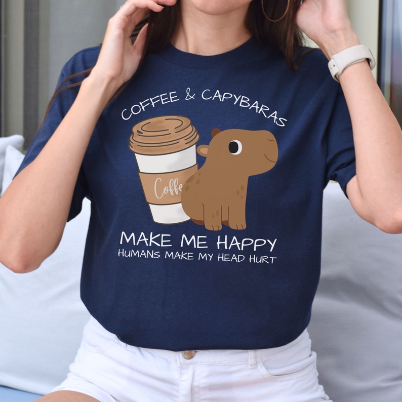 May include: A navy blue t-shirt with a cartoon image of a capybara and a coffee cup. The text on the shirt reads "Coffee & Capybaras Make Me Happy Humans Make My Head Hurt".