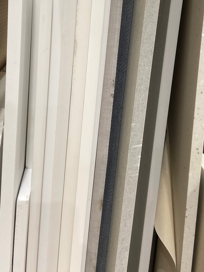 May include: A close-up of a stack of various white and gray boards. The boards are different thicknesses and have a smooth, slightly textured surface.
