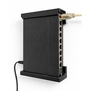 May include: Black NETGEAR network switch mounted on a white wall. The switch has multiple ports and a power cable. A beige network cable is plugged into the side. The word NETGEAR is printed on the front.