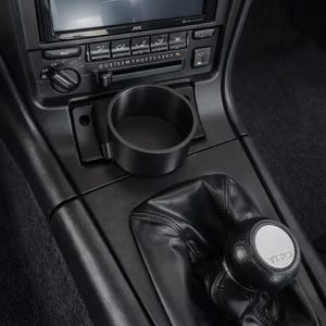 May include: Black car interior with a JVC stereo system, air vents, and a cup holder. The gear shift knob has a silver TRD logo. The dashboard is black.