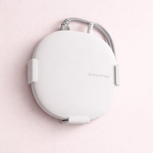 May include: A white, circular SmartThings device with a gray cable and three mounting brackets. The device is mounted on a light pink wall. The SmartThings logo is printed on the device.