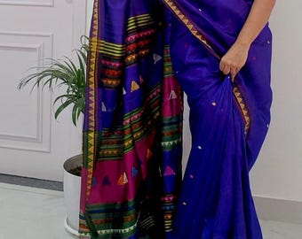 May include: A vibrant blue saree with intricate patterned borders and a decorative edge. The saree features colorful geometric designs in pink, yellow, green, and red. The fabric drapes elegantly, showcasing the detailed craftsmanship and rich color palette.