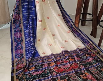 May include: A draped, cream-colored textile with a blue border and intricate patterns. The fabric features floral and geometric designs in shades of blue, red, and purple. The lower portion displays a detailed, multi-colored illustration.