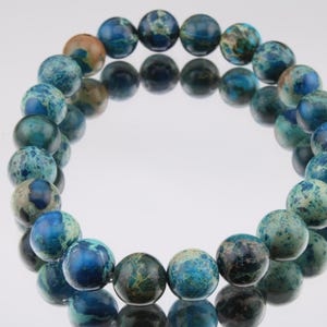 May include: A blue and green jasper beaded bracelet with a round shape. The beads are all the same size and are strung together on a clear elastic cord.